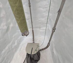 A series of pipes above a trapdoor over a borehole in the million year ice core drilling trench. The tip of the drill barrel is visible above the trapdoor.