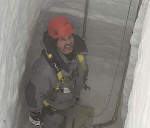 A man standing in a six metre-deep channel dug in show, beside the entry to the borehole for drilling the million year ice core. Two metal pipes that will bring drilling fluid into the borehole are visible extending down the sides of the channel.