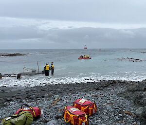 A red IRB loaded with people and cargo is on the water and heads towards a red ship around 500m offshore