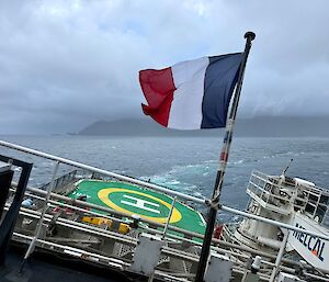 Looking across the front heli-deck of a heavily listing ship to a misty island in the distance.
