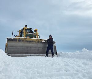 A man standing near a big yellow bulldozer on snow