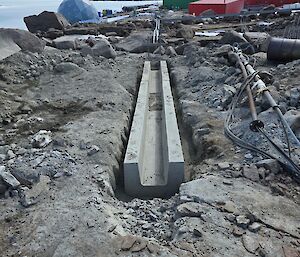 A cement culvert dug into rock with station buildings behind it