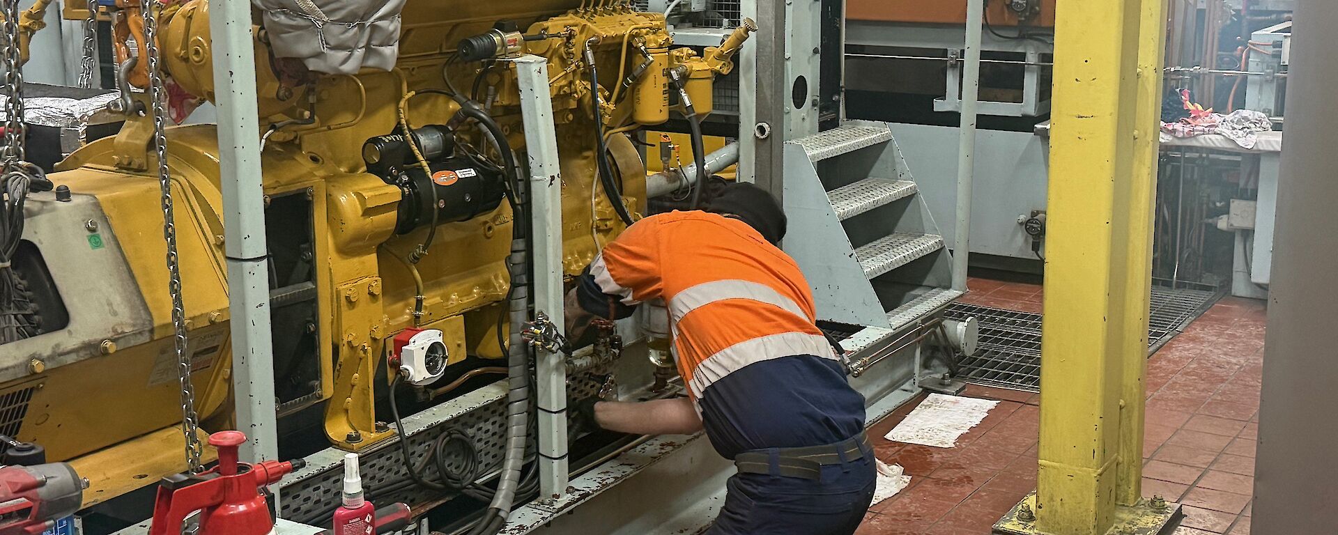 A man wearing high visibility clothing is working on a large yellow generator