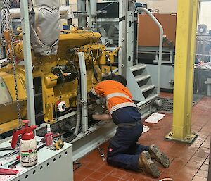 A man wearing high visibility clothing is working on a large yellow generator