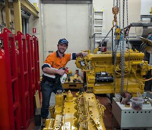 A man in high visibility clothing stands beside a yellow generator that is being held up by a hoist