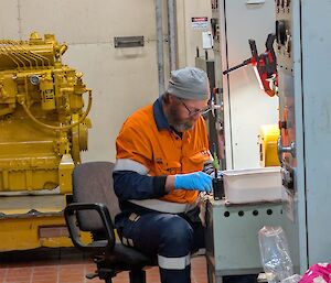 A man in high visibility clothing is undertaking delicate electrical work at a desk