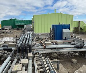 A metal tray filled with cables and pipes is neatly laid out in front of a green and blue building