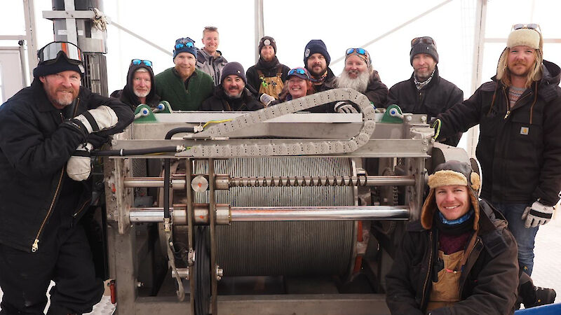 Twelve people standing around a large winch drum.