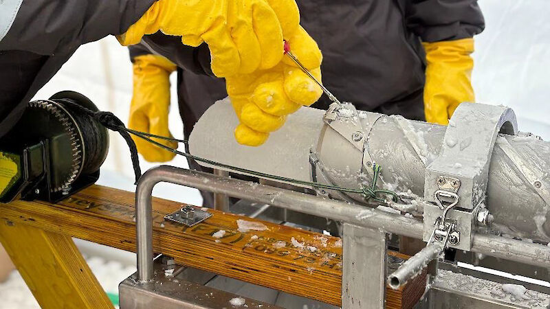 A man trying to loosen part of a drill barrel with a screwdriver, to release an ice core.