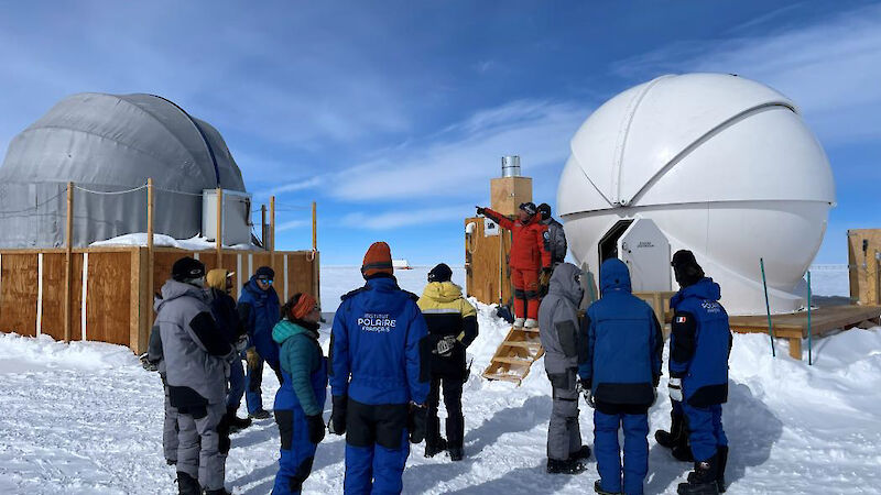 A group of people standing around two domes housing telescopes at Concordia station.