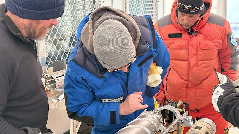 Three men look at the cutting end of an ice core drill barrel