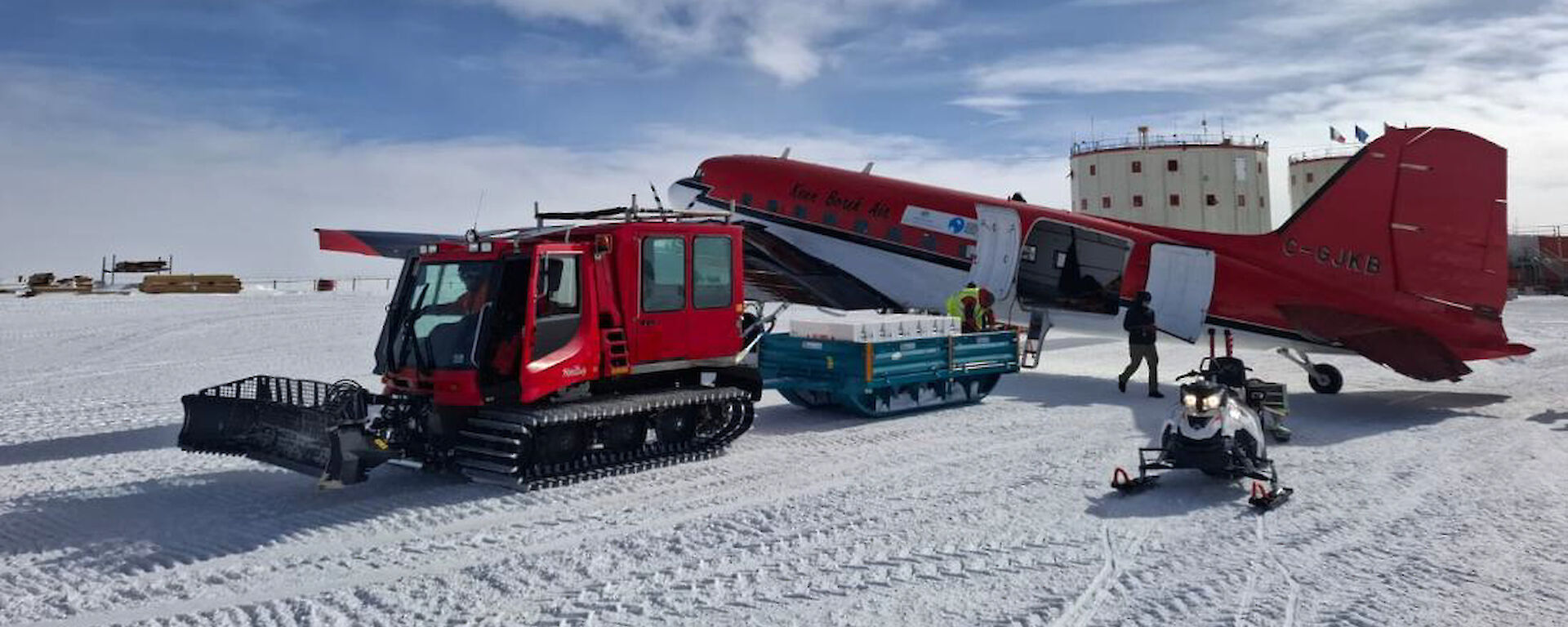 Ice cores are unloaded from a Basler aircraft on to a sled pulled by a red oversnow vehicle at Concordia station.