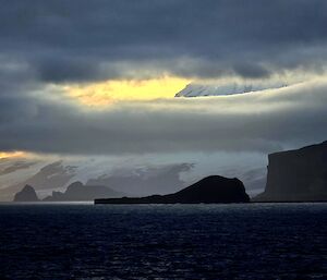 Cloud sweeping across the face of a large snow covered volcano, black cliffs in the foreground