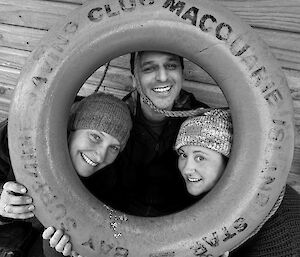 Three smiling people looking through the centre of a life ring