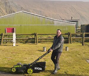 A smiling man mows a lawn with a Ryobi electric lawnmower