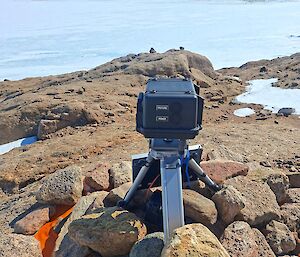 A black camera is mounted inside a rock cairn and is pointing out towards an icy landscape