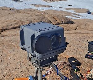 A black camera is mounted inside a rock cairn and is pointing out towards an icy landscape