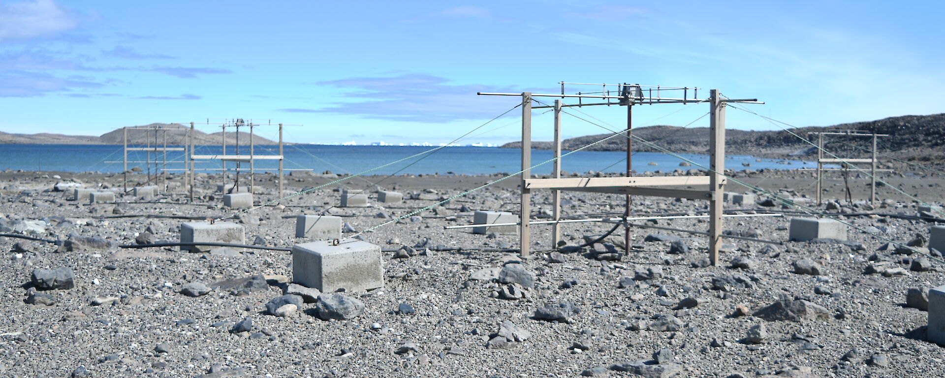 A number of antennas sit in a rocky landscape next to a blue body of water