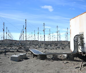 A lot of metal masts, in riderly rows with wires between them extend into the distance, with a beige hut in the foreground. The hut is connected to the array of poles with a very large number of cables laid neatly in trays