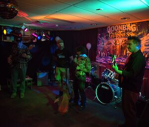 A dimly lit room with musicians playing guitars and drums