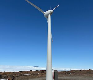 A wind turbine on a gravelly base, surrounded by a brown rocky outcrop