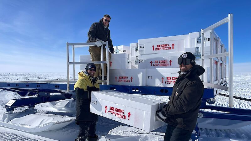 Three men load the back of a sled with white ice core boxes.