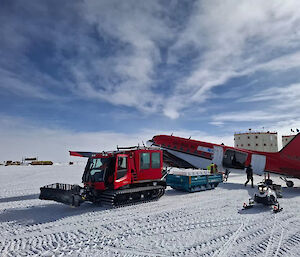 Ice cores are unloaded from a Basler aircraft on to a sled pulled by a red oversnow vehicle at Concordia station.