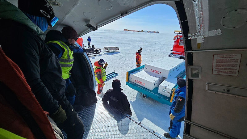 People inside a Basler aircraft waiting for some ice core boxes that are being reversed in a trailer towards the aircraft door.
