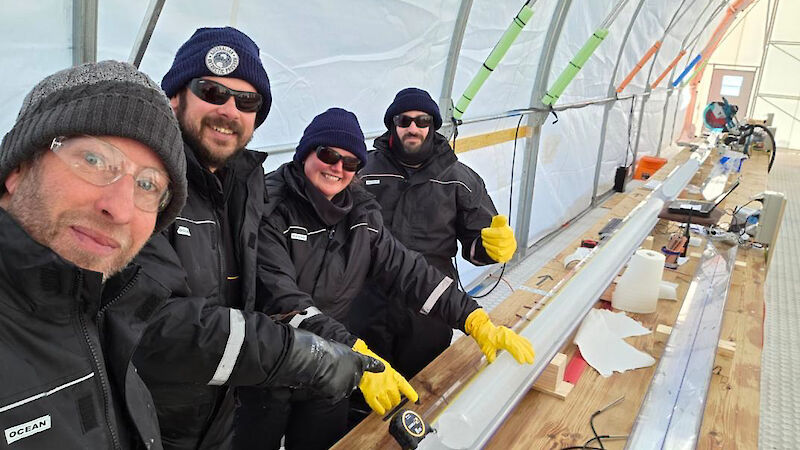 Four people standing beside a three metre-long ice core on a bench.