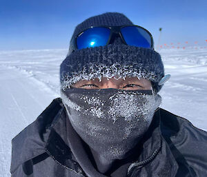 A woman with her face almost complete covered, except for her eyes, with a beanie and face/neck warmer, which are both encrusted with ice.
