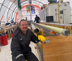 A man kneeling at the end of a long ice core drill barrel.