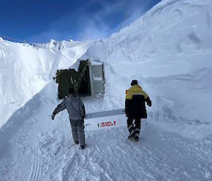 Two people carrying a box of ice cores inside a deep snow trench.