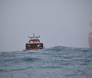 A small orange boat at sea next to a large red ship