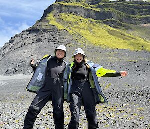 Two wome in black outfits wearing sunhats, standing smiling on grey rocky earth
