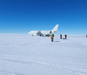 An Airbus aircraft on a snow runway, with a few people walking away from it, towards the camera.