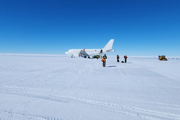 An Airbus aircraft on a snow runway, with a few people walking away from it, towards the camera.