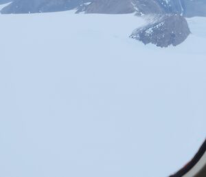 View from an aircraft windown towards the pointed rocky peaks of a mountain range, projecting above the deep snow.