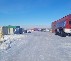 An image of Casey station, with a large red building on the right behind a large red vehicle, with shipping containers on the left.