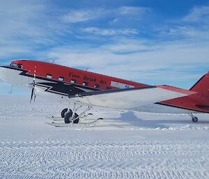 A red aircraft on a plowed snowfield.