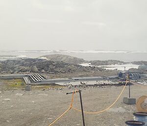 Looking through a window, the image is of the bay off Casey station, with water and snowy hills in the background.