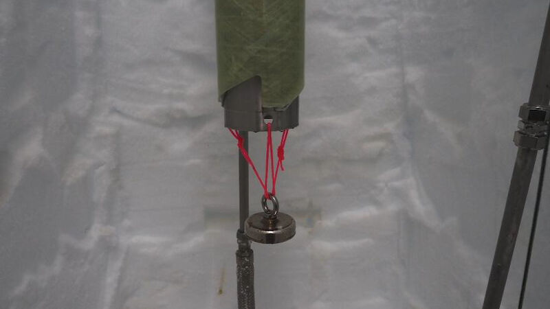 A circular magnet attached by thin red cord to the bottom of the ice core drill barrel.