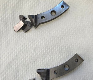 Two small pieces of metal sitting beside two larger pieces, off which they broke.