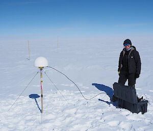 A woman standing beside a GPS station - a white top shaped like half an egg, on a pole.