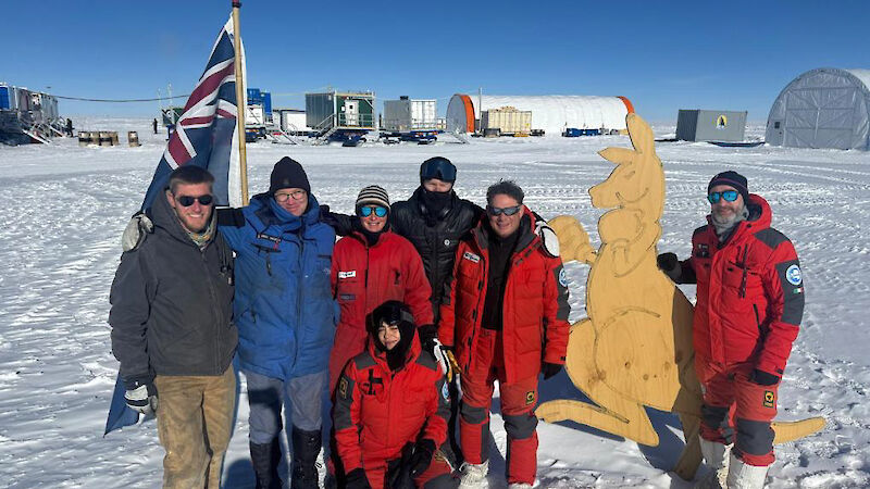 A group of people standing beside an Australian flage and a wooden cutout of a boxing kangaroo.