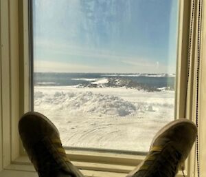 Adam's feet in the foreground, rested on the upper wallow window sill, the view of snow, a rocky hill and Newcomb Bay beyond