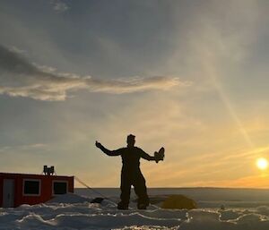 Amber standing in the foreground, with the orange survival shelter and a lovely sunrise in the background