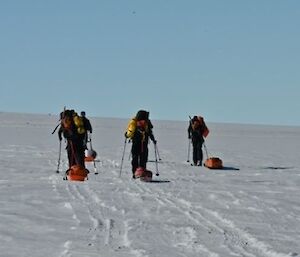 Four skiers towing sleds on an uphill slope of snow.