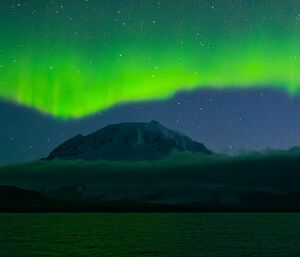 Green shimmering light over a snow capped volcano with stars everywhere