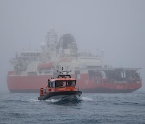 A small orange boat on the sea with Australia's icebreaker behind it