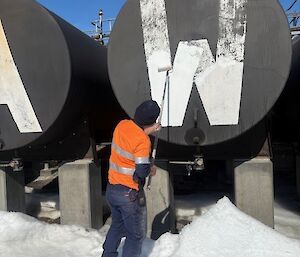 A man uses a paint roller to reapply white paint to the 'W' letter on the Mawson station sign.